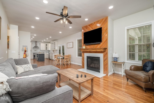 living area featuring a large fireplace, a ceiling fan, recessed lighting, light wood finished floors, and baseboards