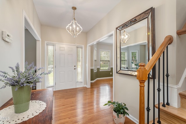 foyer entrance featuring stairway, baseboards, an inviting chandelier, and wood finished floors