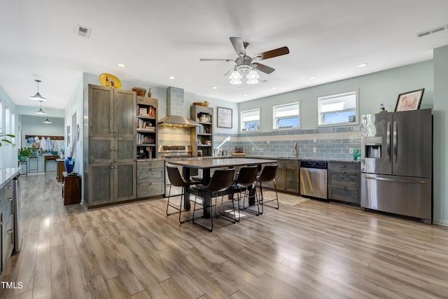 kitchen featuring ceiling fan, wall chimney range hood, open shelves, appliances with stainless steel finishes, and decorative backsplash