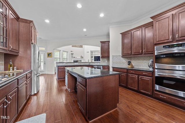 5928 Terrington Ln, Raleigh, NC 27606 - kitchen featuring glass insert cabinets, arched walkways, dark wood finished floors, stainless steel appliances, and a kitchen island