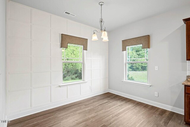 spare room featuring wood finished floors, healthy amount of natural light, baseboards, and a chandelier
