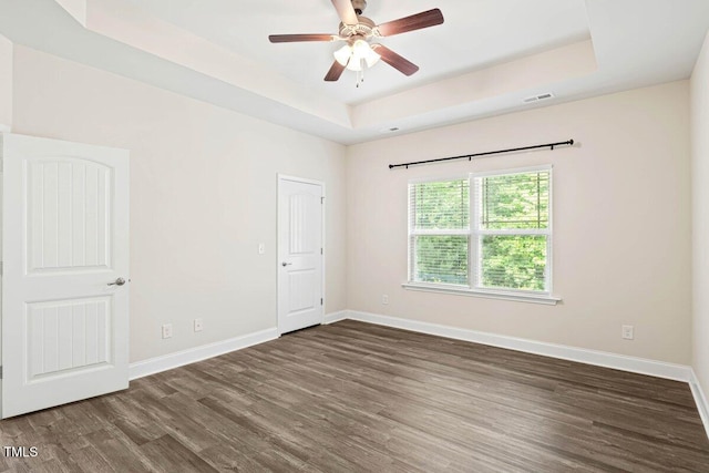 spare room featuring a raised ceiling, wood finished floors, baseboards, and a ceiling fan