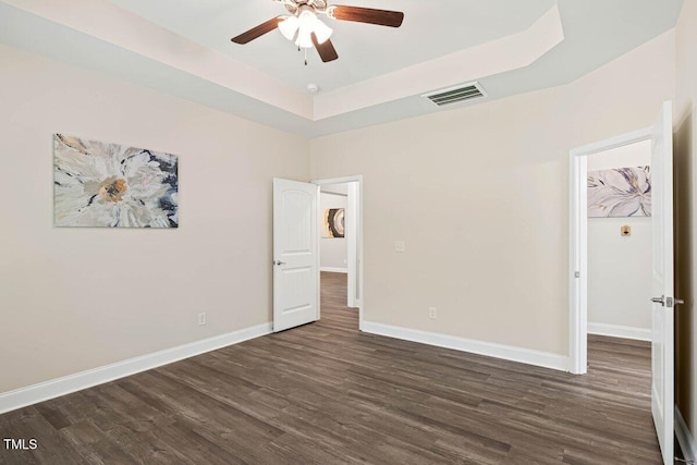 unfurnished bedroom with a raised ceiling, dark wood-style flooring, baseboards, a walk in closet, and a ceiling fan