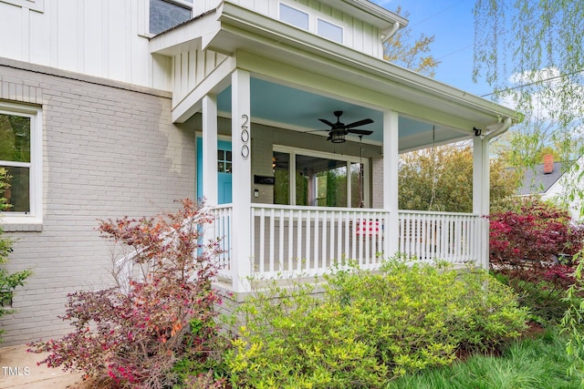 view of exterior entry featuring a porch, board and batten siding, a ceiling fan, and brick siding