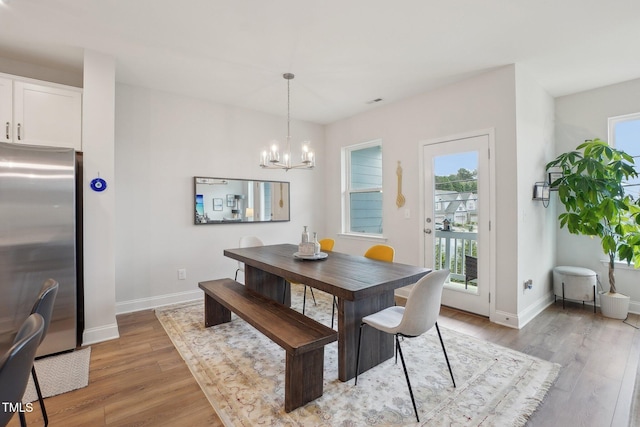 dining room with light wood-type flooring, a notable chandelier, and baseboards