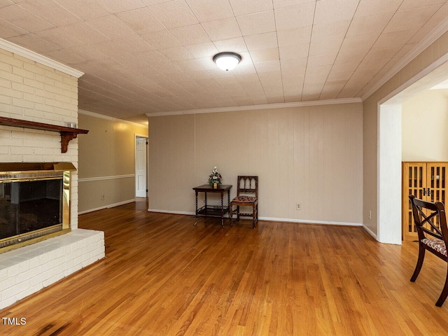 unfurnished living room with crown molding, wood finished floors, baseboards, and a brick fireplace
