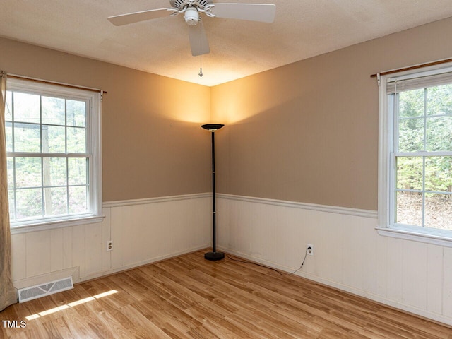 unfurnished room with visible vents, a wealth of natural light, wainscoting, and wood finished floors