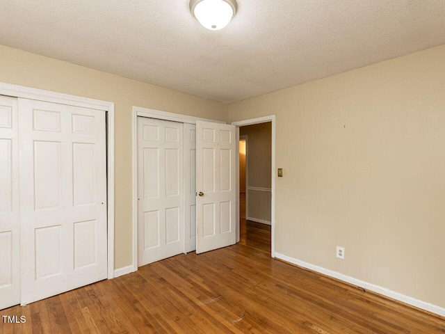 unfurnished bedroom featuring wood finished floors, baseboards, and multiple closets