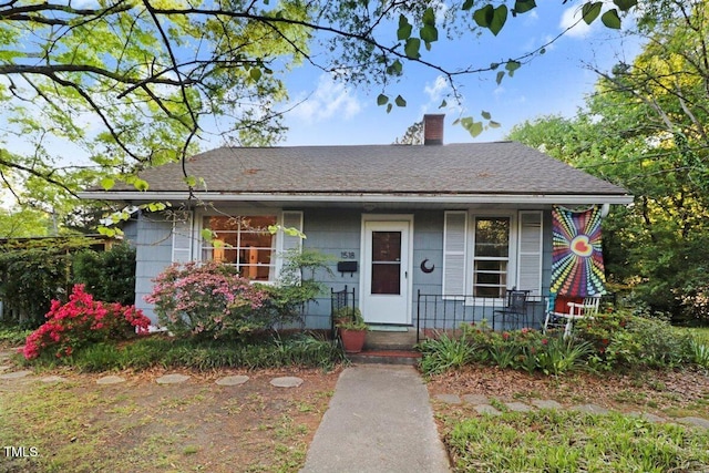 bungalow-style house featuring a chimney, roof with shingles, and covered porch