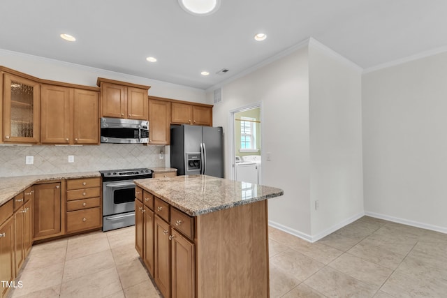 113 Dowington Ln, Cary, NC 27519 - kitchen with appliances with stainless steel finishes, washer and dryer, brown cabinetry, decorative backsplash, and light stone counters