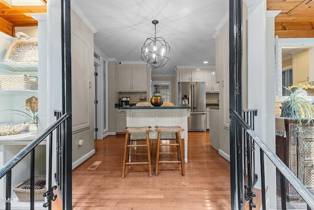 kitchen featuring stainless steel refrigerator with ice dispenser, a kitchen island, crown molding, dark countertops, and light wood-style flooring