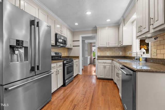 kitchen with appliances with stainless steel finishes, a sink, white cabinetry, crown molding, and light wood-style floors