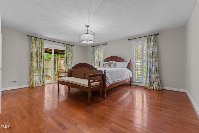 bedroom with wood finished floors, baseboards, a textured ceiling, and a chandelier