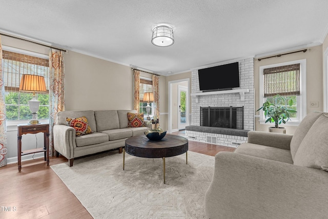 living area featuring crown molding, wood finished floors, healthy amount of natural light, a brick fireplace, and a textured ceiling