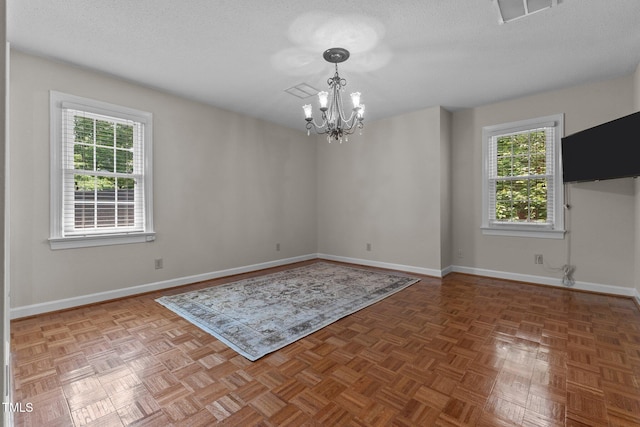 unfurnished room with a chandelier, healthy amount of natural light, baseboards, and a textured ceiling