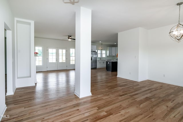 unfurnished living room with a chandelier, light wood finished floors, a ceiling fan, and baseboards