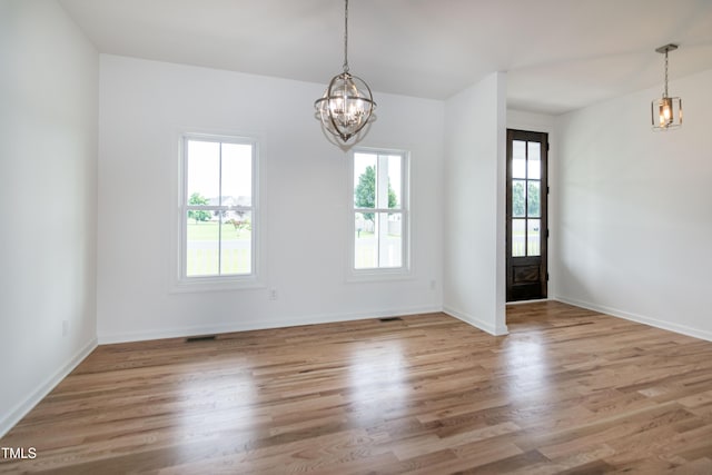 unfurnished dining area with healthy amount of natural light, a chandelier, wood finished floors, and baseboards