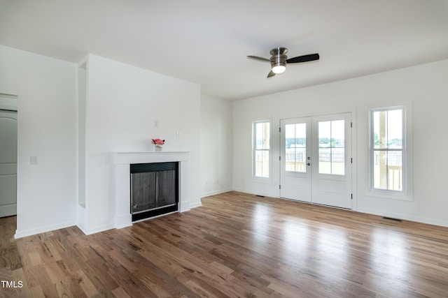 unfurnished living room with a ceiling fan, a fireplace, wood finished floors, and french doors