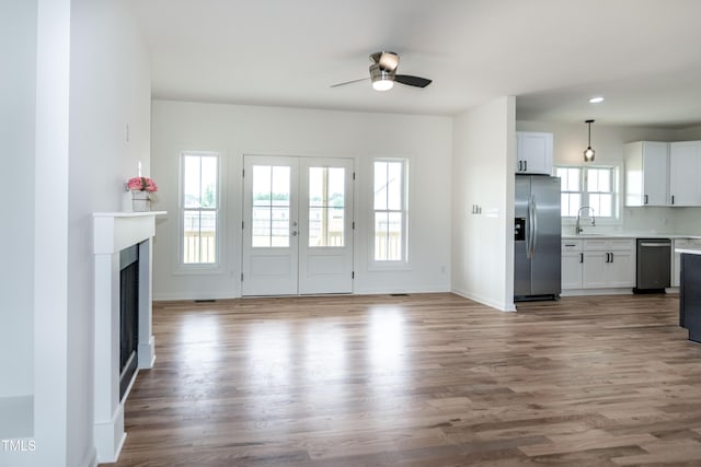 unfurnished living room with a ceiling fan, wood finished floors, a fireplace, baseboards, and a sink