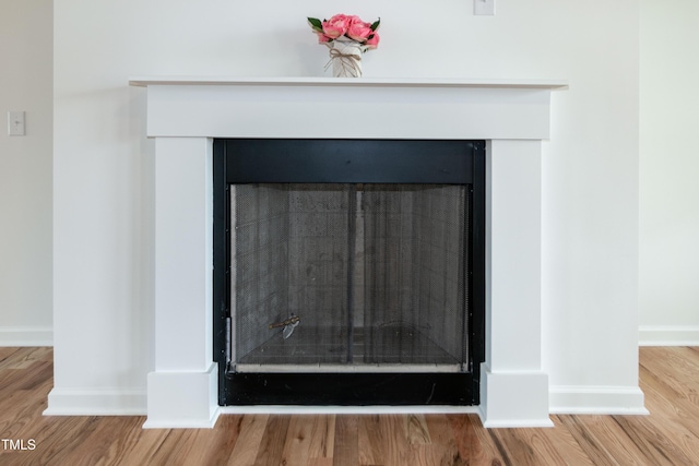 detailed view of a fireplace, wood finished floors, and baseboards