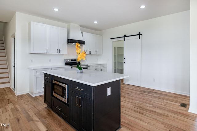 kitchen featuring stainless steel appliances, custom exhaust hood, light wood-style flooring, a barn door, and recessed lighting