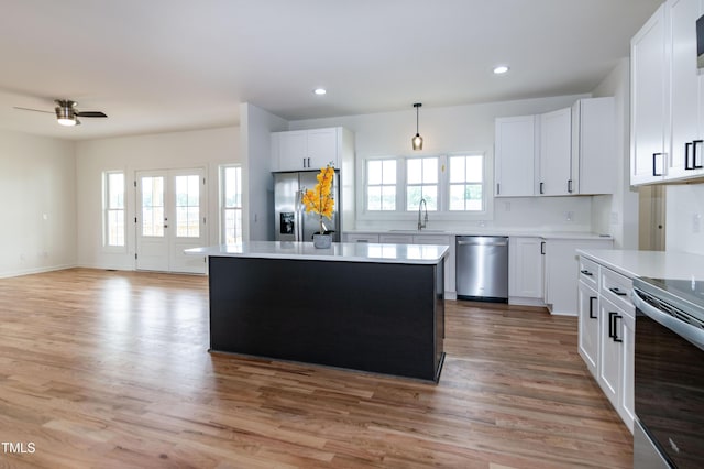 kitchen with appliances with stainless steel finishes, a sink, light wood-style flooring, ceiling fan, and a center island