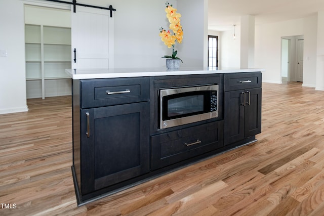 detailed view of stainless steel microwave, wood finished floors, baseboards, and a barn door