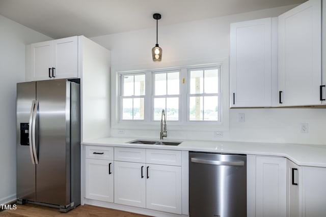 kitchen featuring stainless steel appliances, a sink, white cabinetry, light countertops, and hanging light fixtures