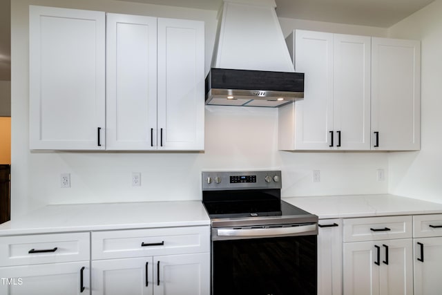 kitchen with stainless steel electric range, wall chimney exhaust hood, white cabinetry, and light countertops