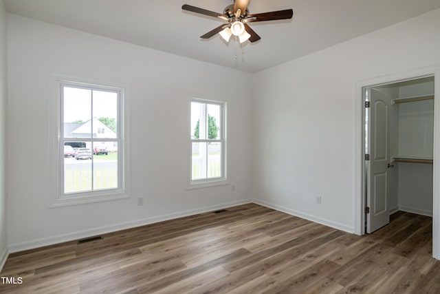 unfurnished bedroom with wood finished floors, a spacious closet, baseboards, a closet, and ceiling fan