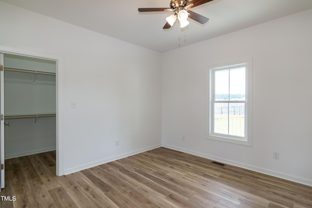 unfurnished bedroom featuring wood finished floors, a spacious closet, baseboards, and a closet