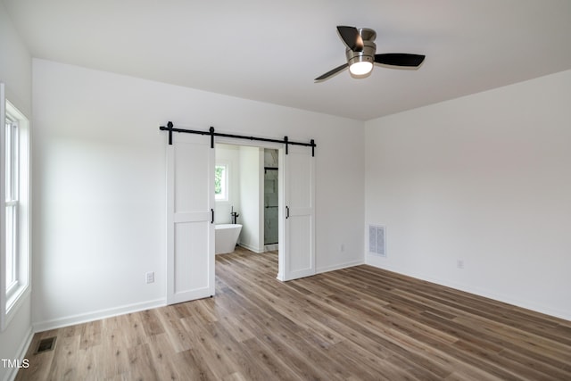 empty room with a barn door, ceiling fan, light wood-style flooring, and baseboards