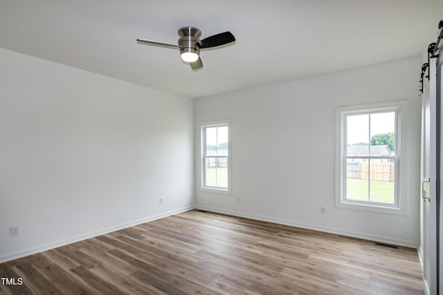 empty room featuring a barn door, plenty of natural light, wood finished floors, and ceiling fan