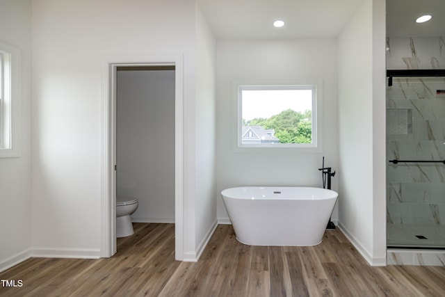 bathroom featuring a stall shower, wood finished floors, toilet, a freestanding tub, and baseboards