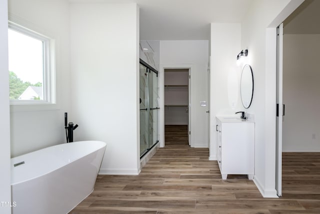 bathroom featuring a stall shower, wood finished floors, vanity, a freestanding bath, and baseboards