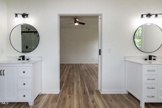 bathroom featuring ceiling fan, wood finished floors, baseboards, and two vanities