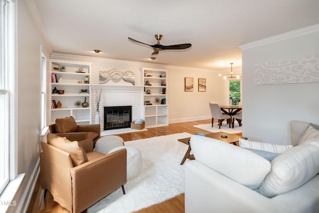 living area with baseboards, light wood-style floors, ceiling fan with notable chandelier, a fireplace, and ornamental molding