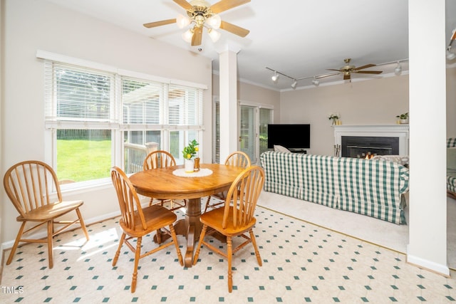 dining area featuring ceiling fan, track lighting, plenty of natural light, a warm lit fireplace, and crown molding