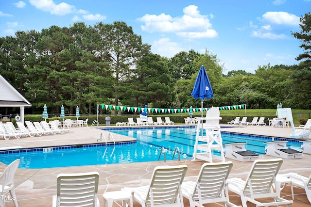 community pool with a patio area, fence, and view of scattered trees