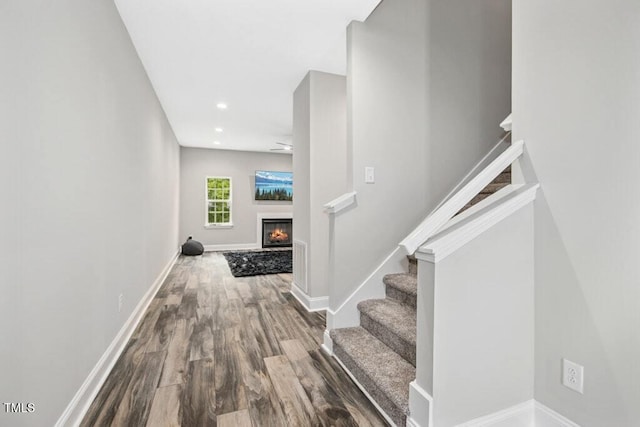interior space with baseboards, recessed lighting, wood finished floors, and a warm lit fireplace