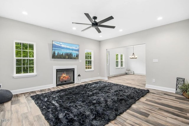 living area featuring light wood-style flooring, ceiling fan with notable chandelier, recessed lighting, baseboards, and a fireplace with flush hearth