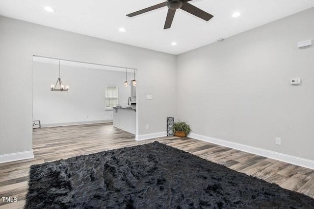 empty room featuring light wood-type flooring, a sink, baseboards, ceiling fan with notable chandelier, and recessed lighting