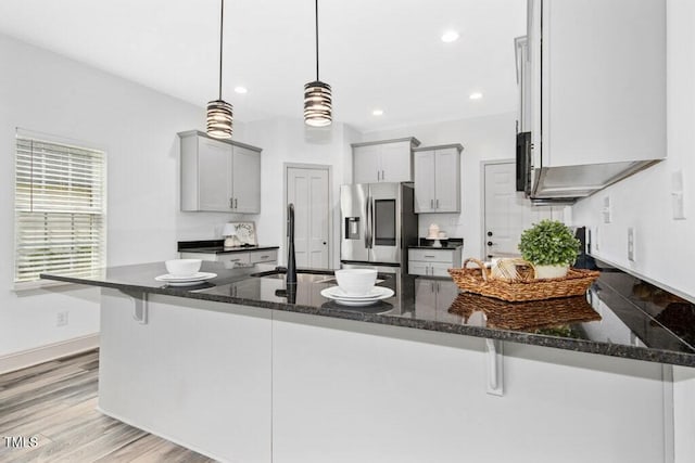 kitchen with a breakfast bar, stainless steel fridge, gray cabinets, dark stone counters, and a peninsula