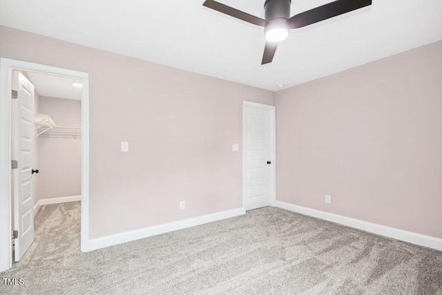 unfurnished bedroom with a closet, baseboards, ceiling fan, a spacious closet, and carpet flooring