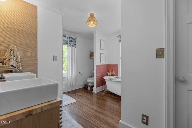 bathroom featuring wood finished floors, vanity, a freestanding tub, baseboards, and ornamental molding