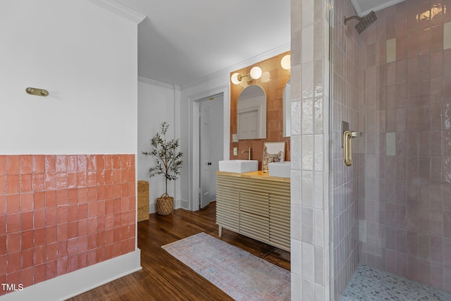 bathroom with wood finished floors, vanity, ornamental molding, and a tile shower