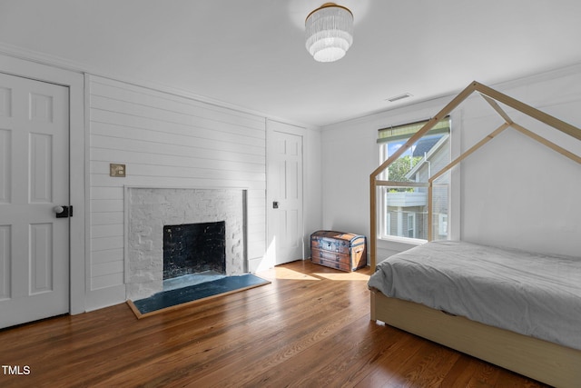bedroom with ornamental molding, wood finished floors, visible vents, and a fireplace