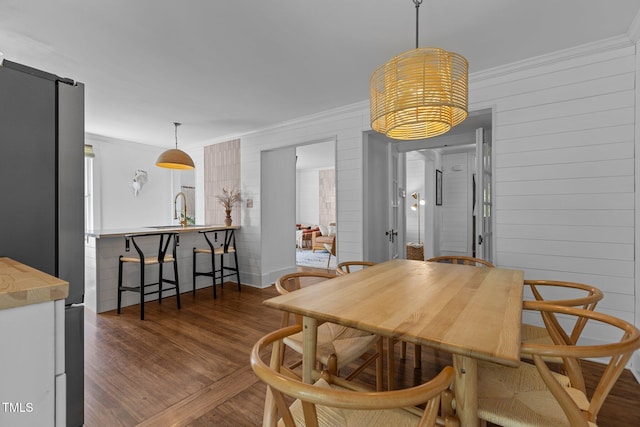 dining space with dark wood-style flooring, ornamental molding, wood walls, and an inviting chandelier