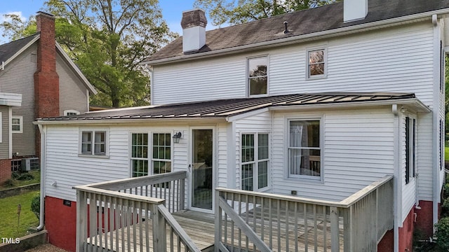 back of property with a chimney, a deck, cooling unit, metal roof, and a standing seam roof