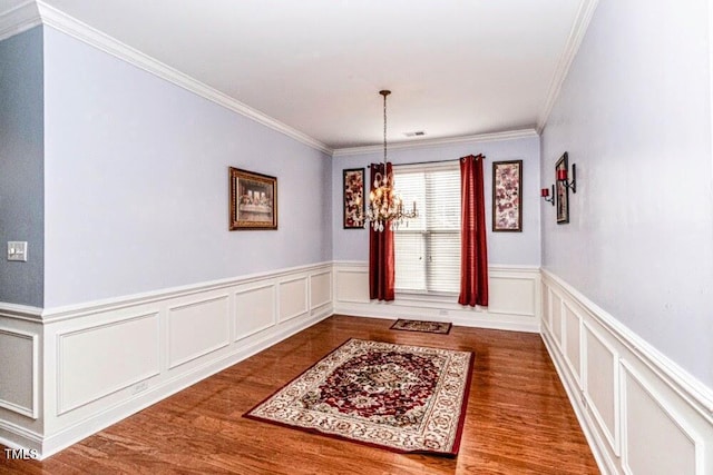 dining room with a decorative wall, visible vents, wood finished floors, wainscoting, and a notable chandelier